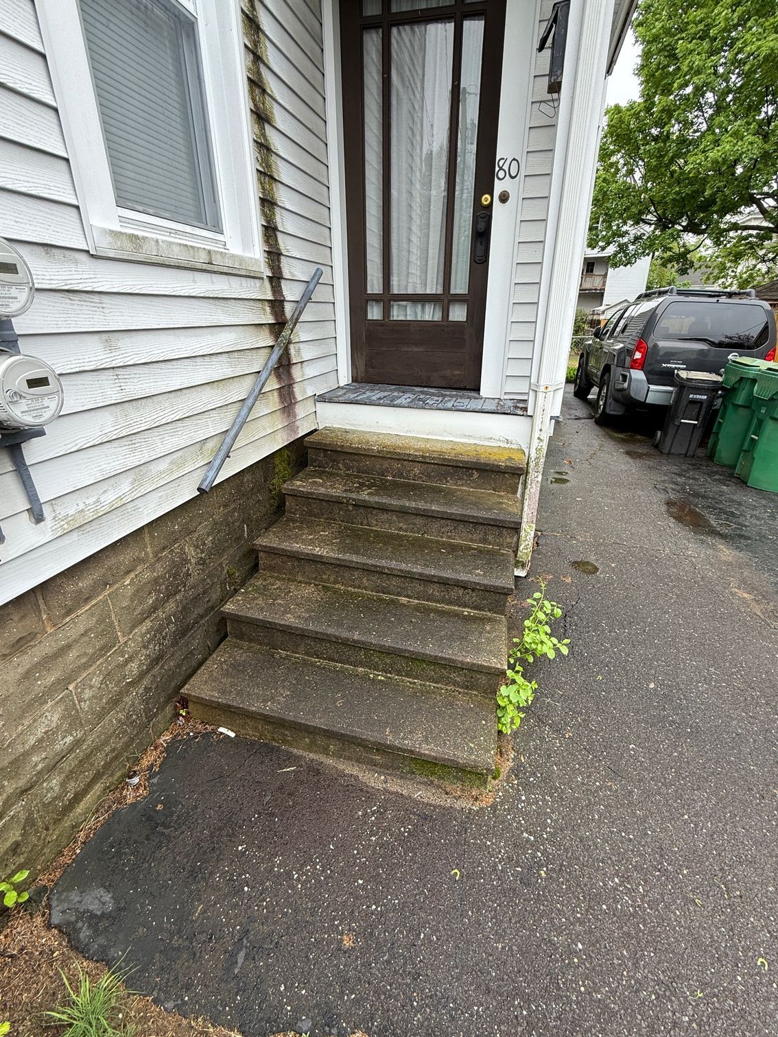 Concrete steps leading up to a front door with a glass window panel. A metal railing is affixed to the house.