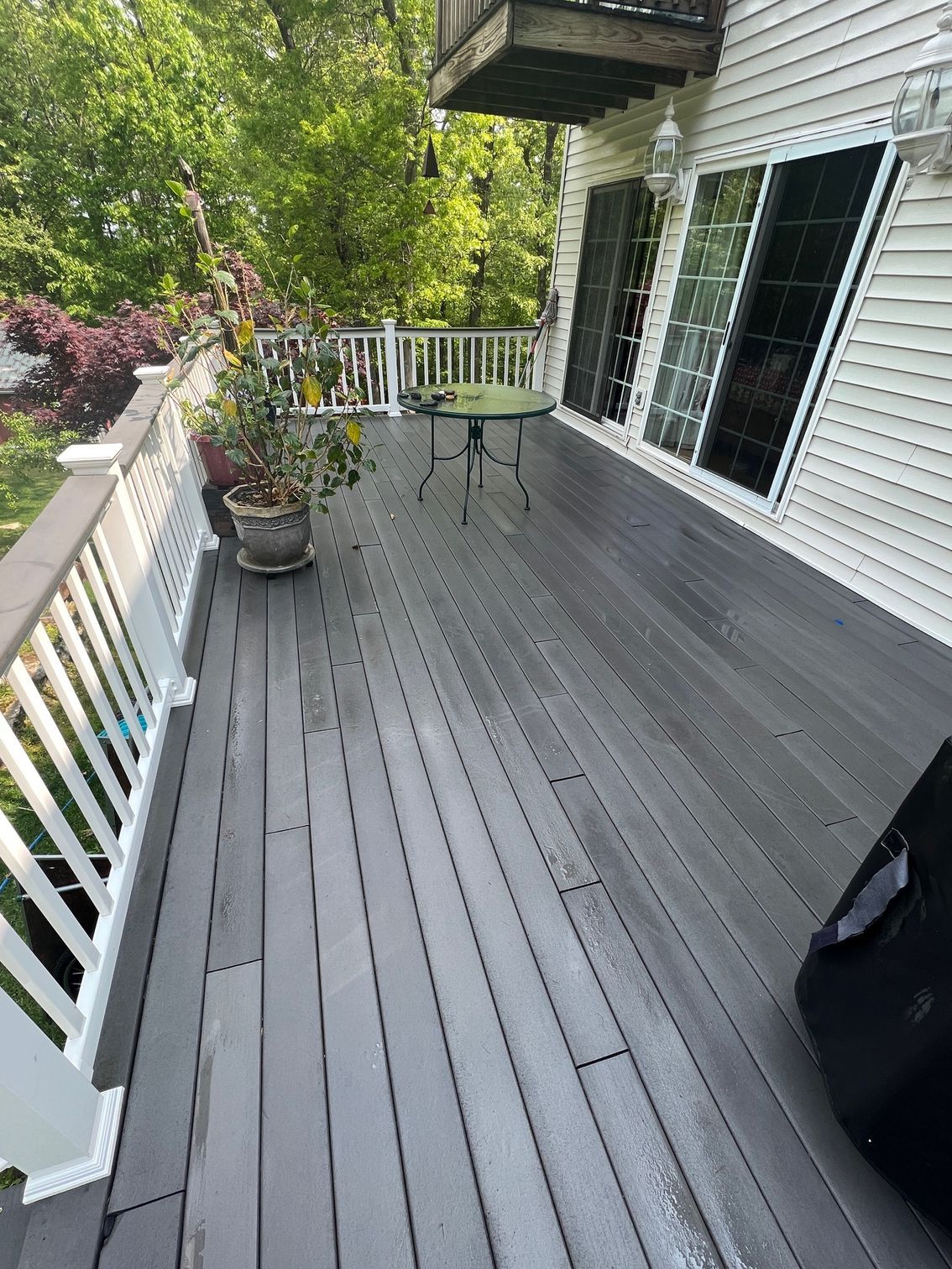 Gray deck with white railing, potted plant, small table, and sliding glass door.