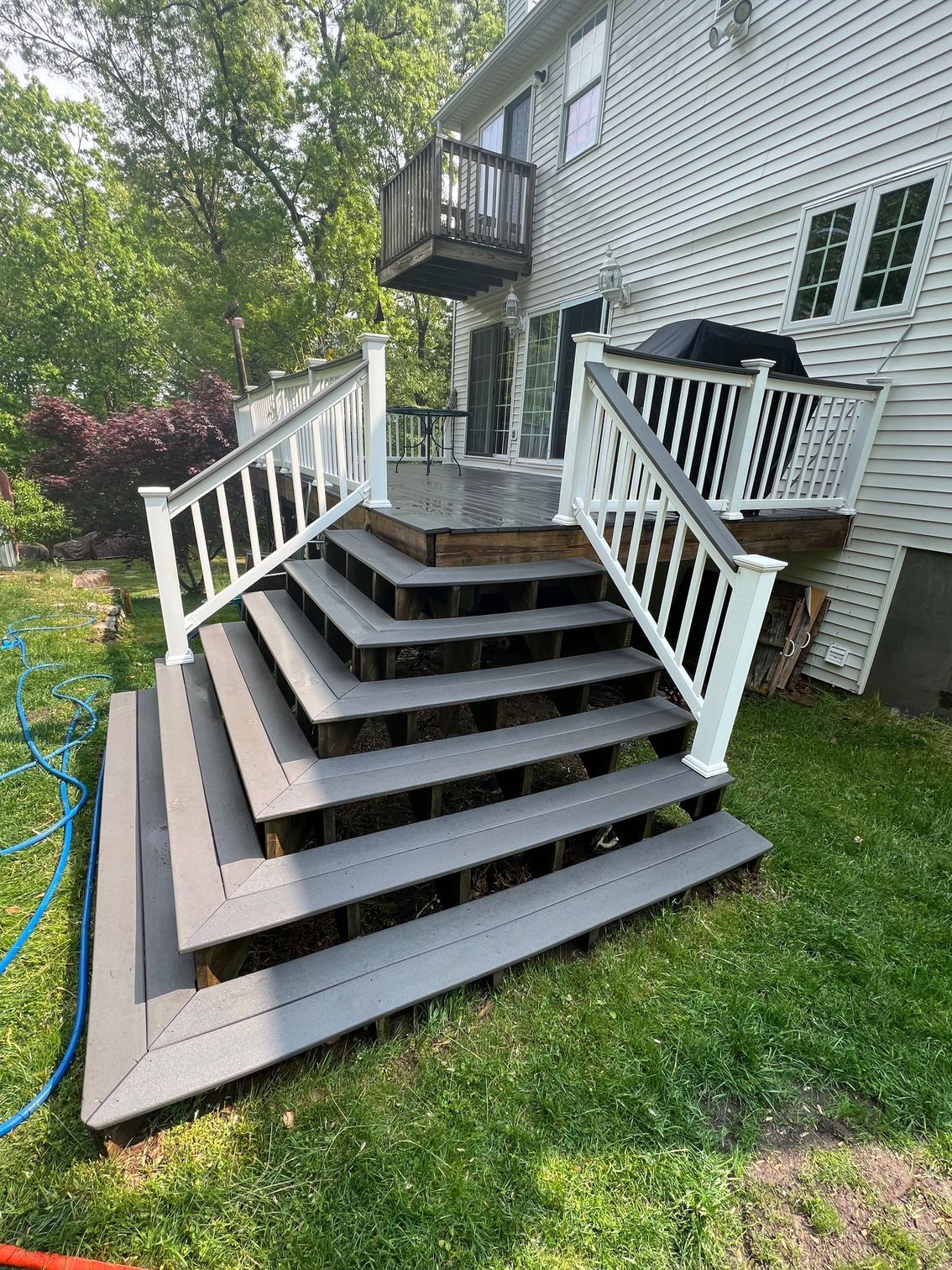 Gray composite deck with white railing and steps leading to a house. Green grass surrounds it.