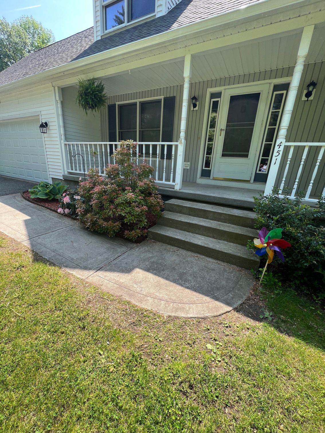 A house with a porch and stairs and a pinwheel in front of it.