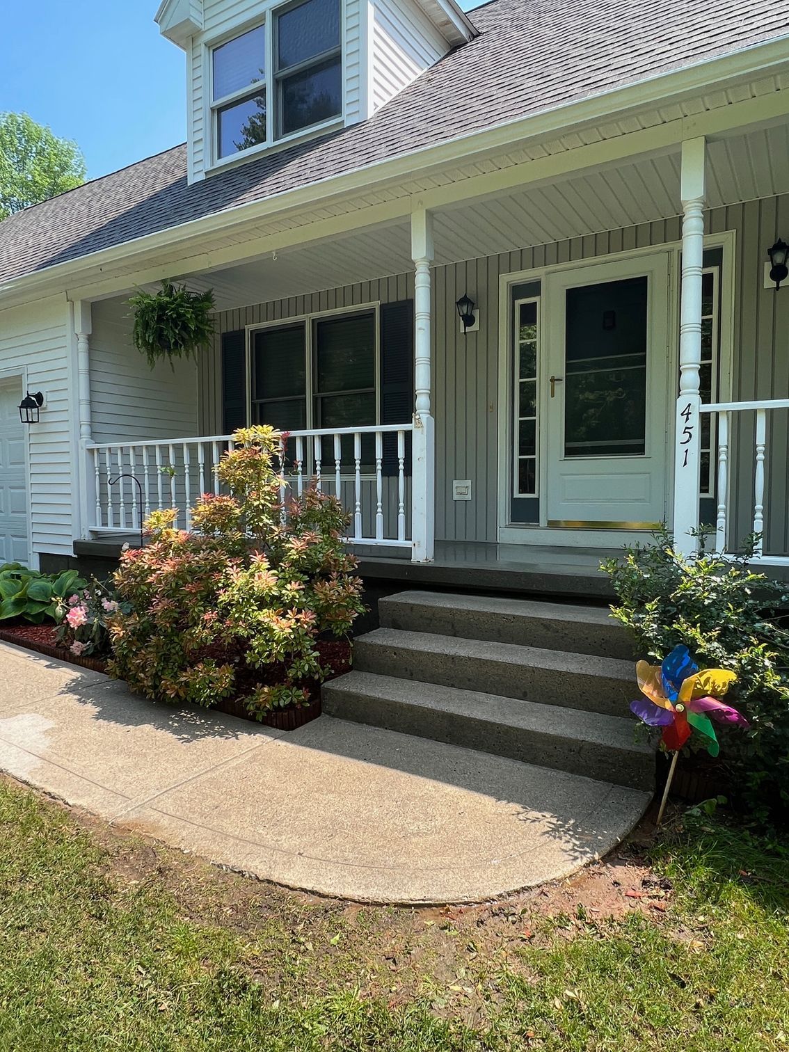 A light gray house with a porch, concrete steps, and a curved walkway. A colorful pinwheel sits to the right.