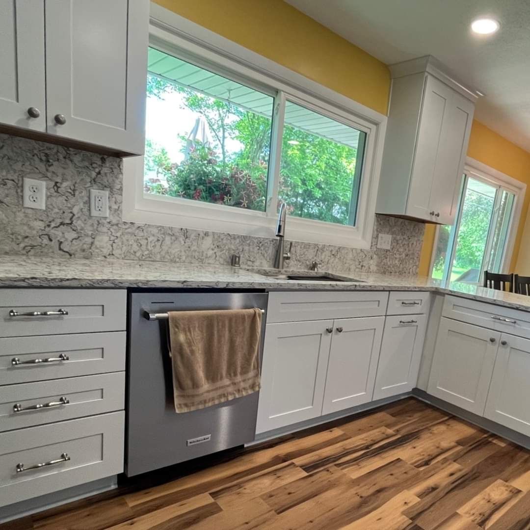 White kitchen cabinets, stainless steel dishwasher, granite countertops, and wood floors.