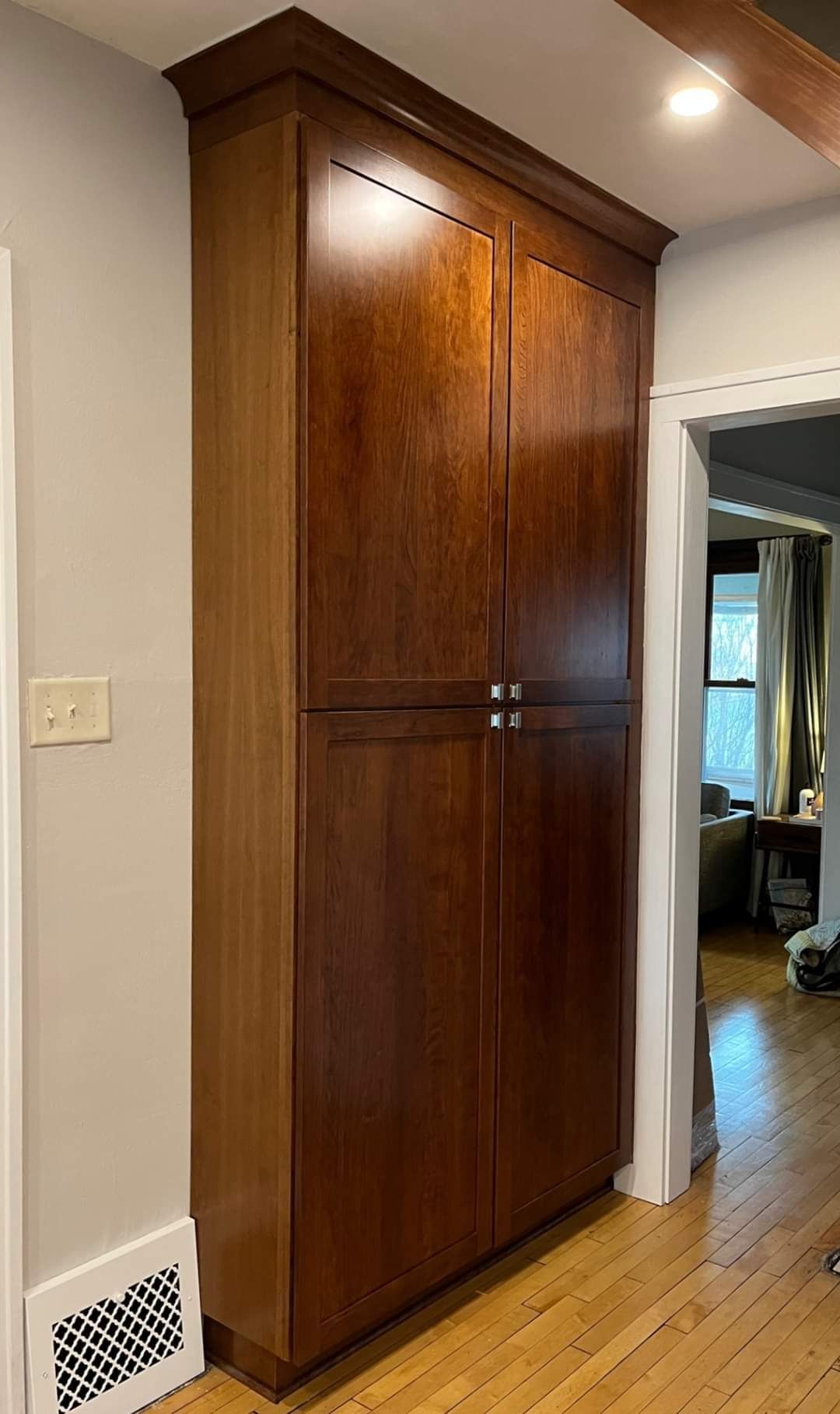 Tall, dark-stained wooden pantry cabinet with four doors, built-in to the wall in a kitchen.