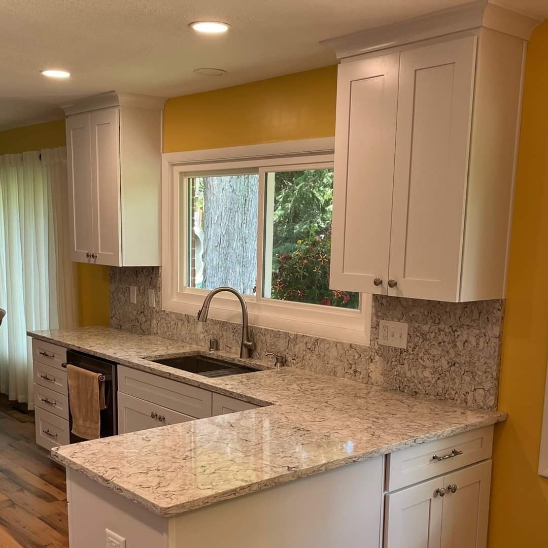 White kitchen cabinets with granite countertops, stainless steel sink under a window, and yellow wall.