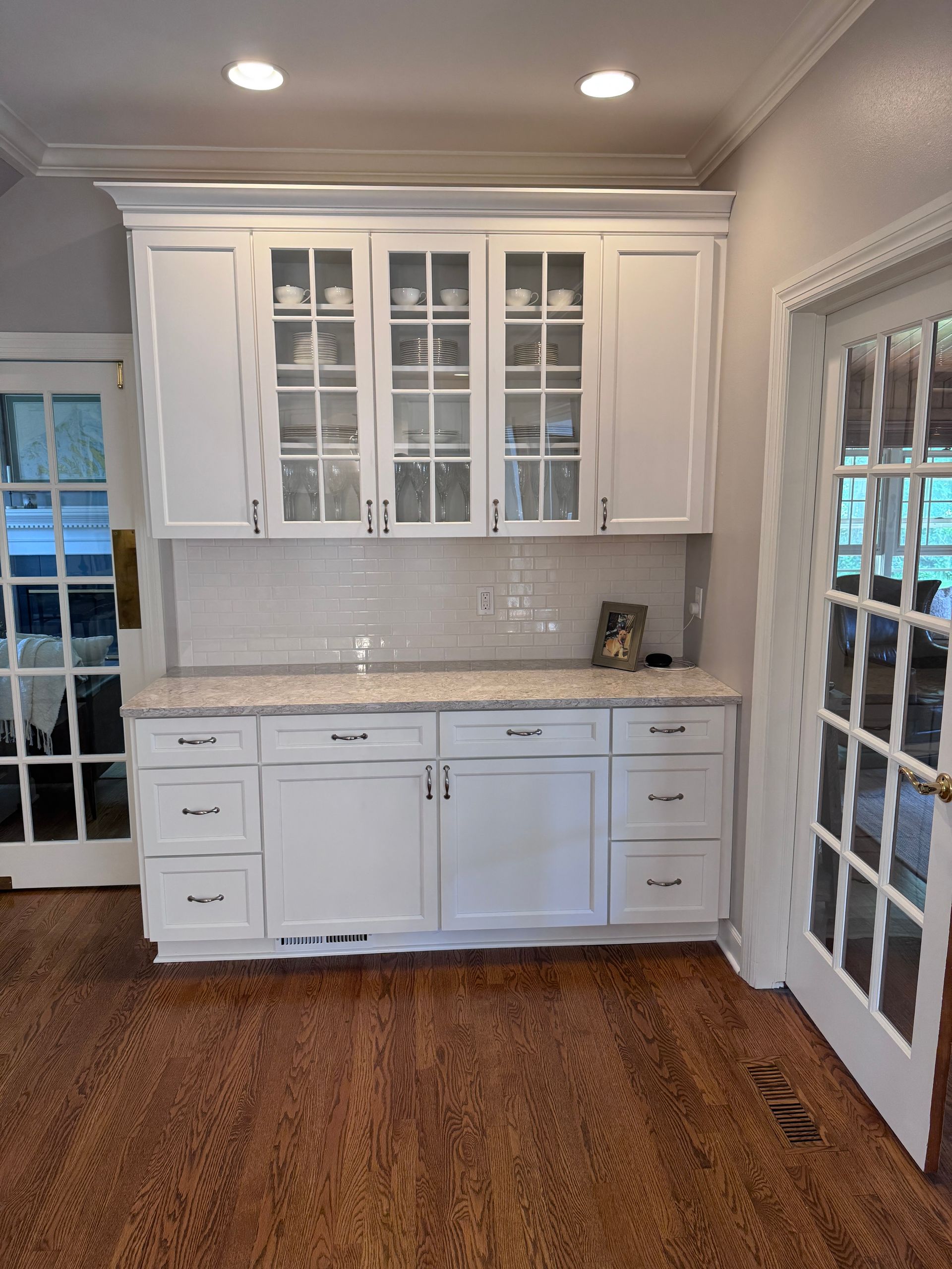 White kitchen cabinets with glass doors, granite countertop, and wood floor.