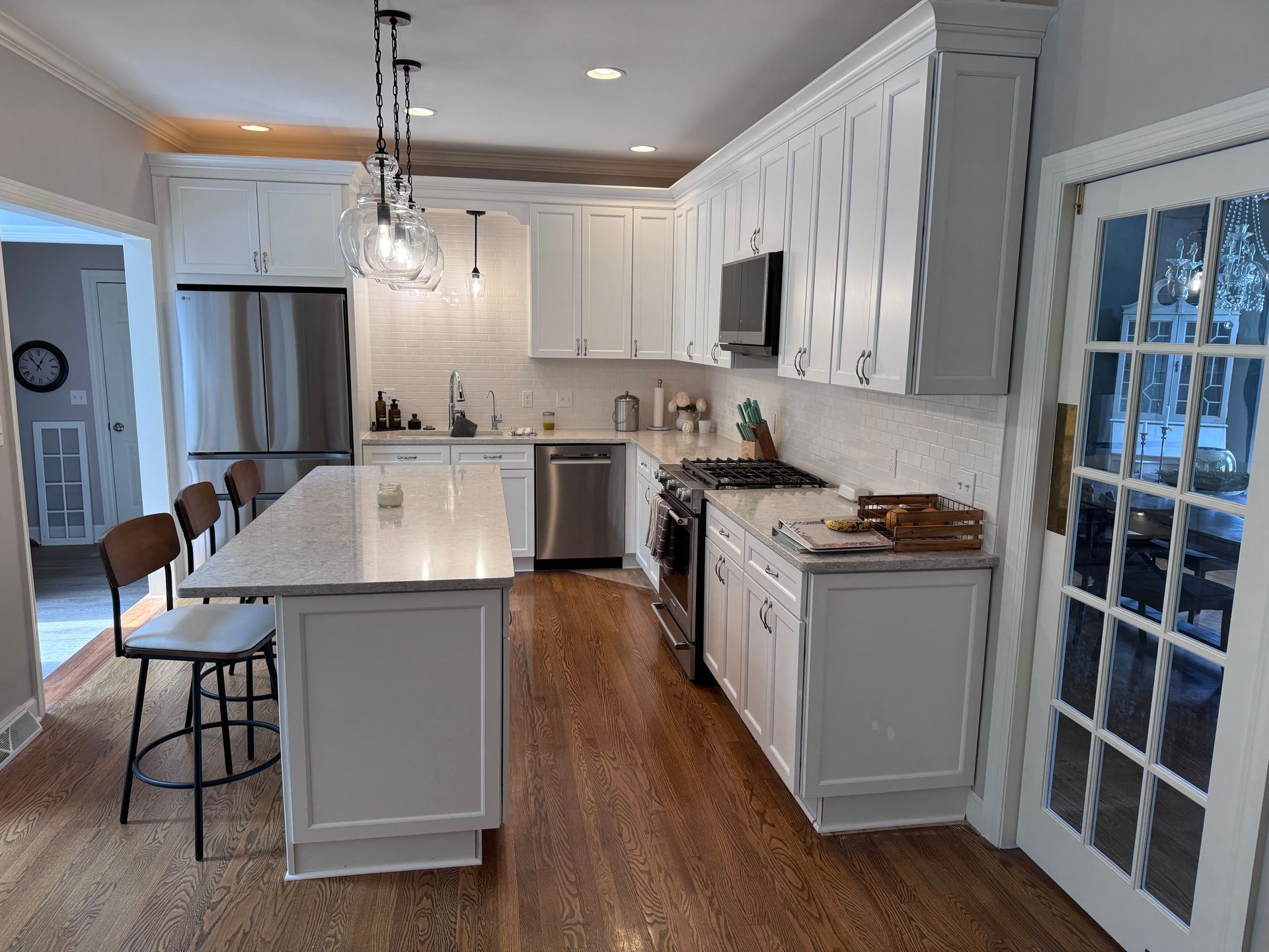 White kitchen with island, stainless steel appliances, and hardwood floors.