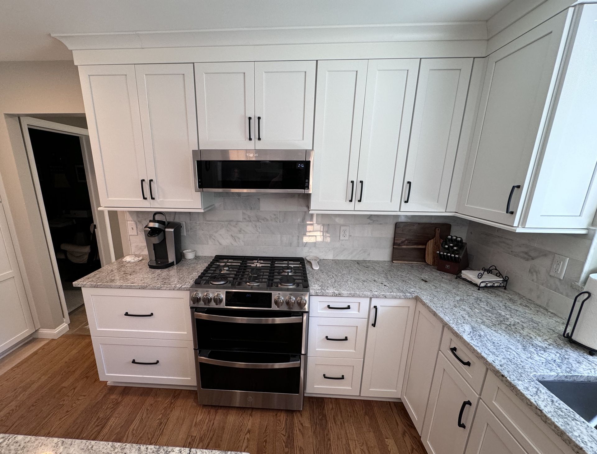 White kitchen cabinets with black hardware, stainless steel appliances, and granite countertops.