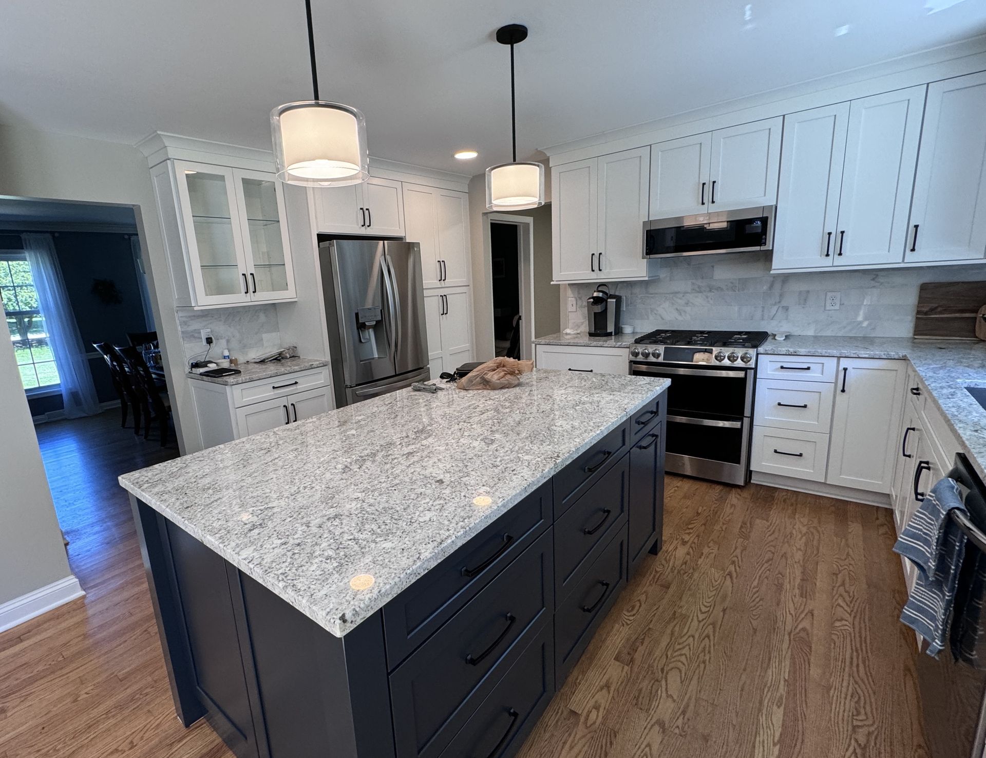 Spacious kitchen with a dark blue island, white cabinets, stainless steel appliances, and granite countertops.
