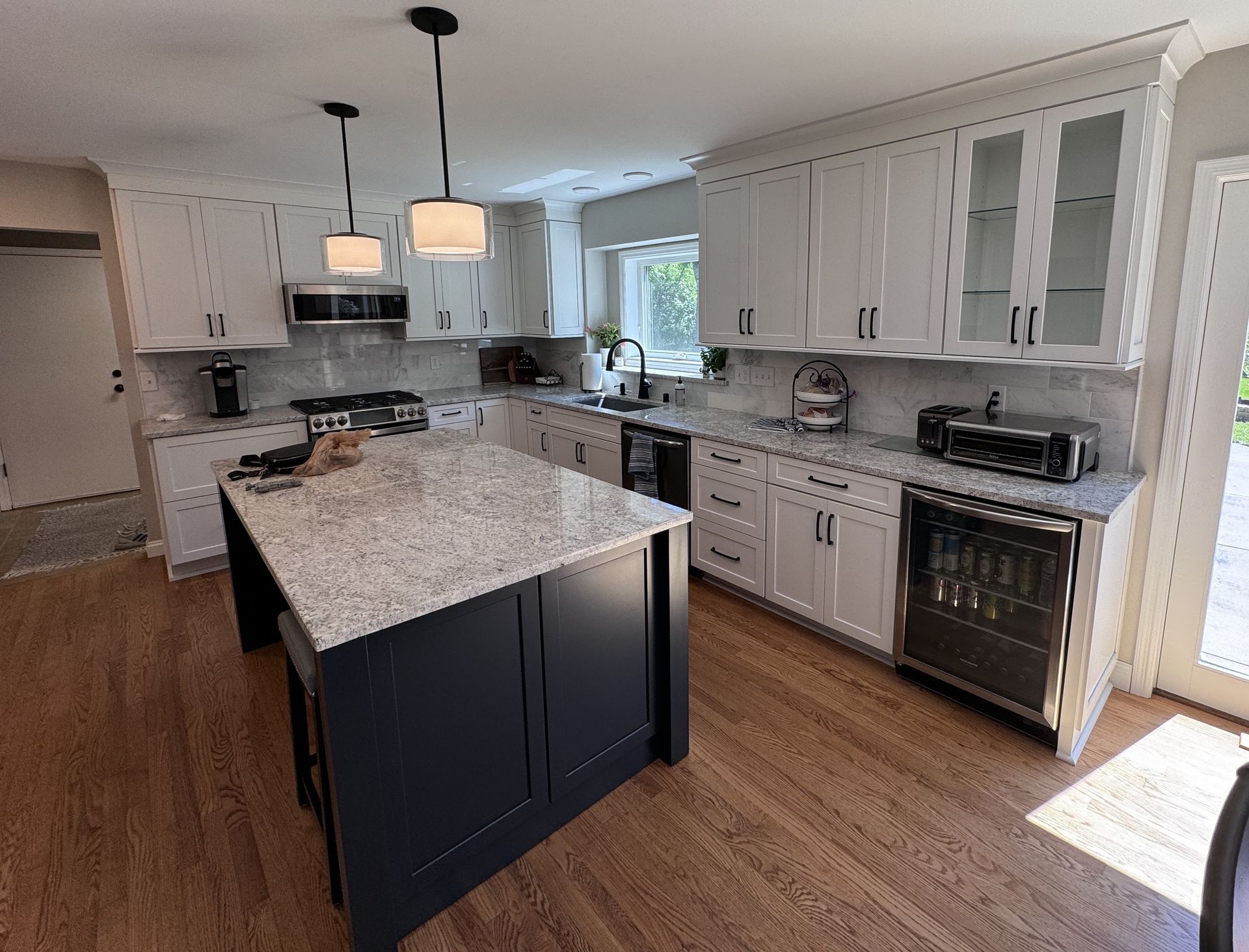 Modern kitchen with white cabinets, dark island, granite countertops, and wood floors.