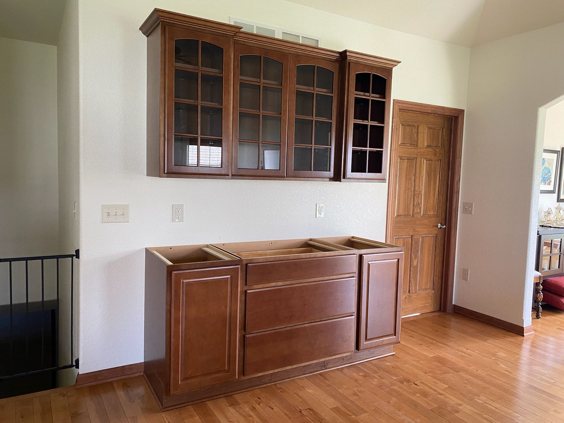 Brown kitchen cabinets mounted on the wall, door and stairs in background.