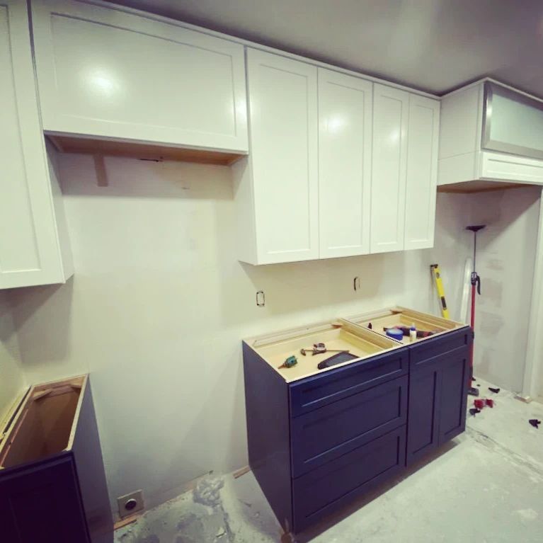 Kitchen renovation: white upper cabinets, dark blue base cabinets, and unfinished wall.