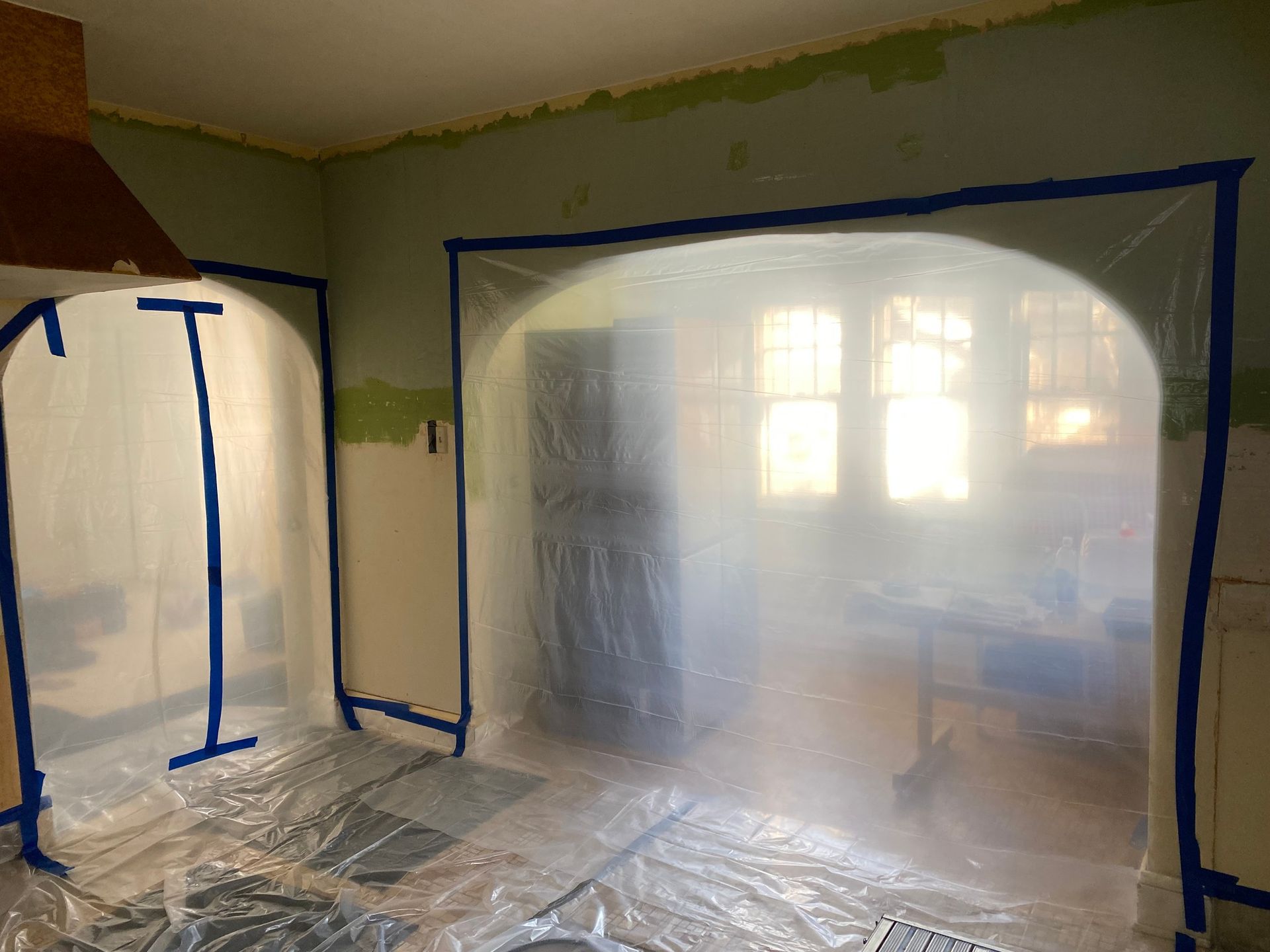 Kitchen renovation in progress, walls and openings taped and covered with plastic sheeting.