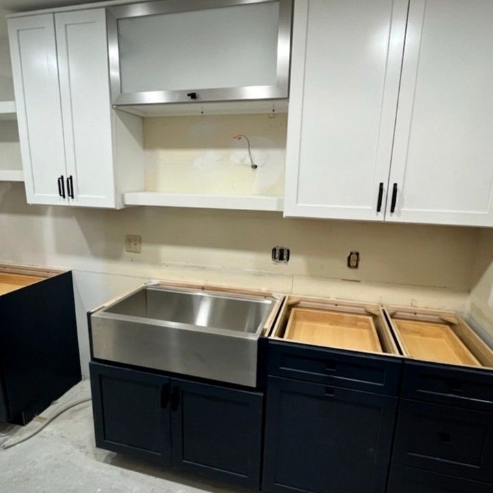 Kitchen under construction with white upper cabinets and navy blue lower cabinets, stainless steel sink.