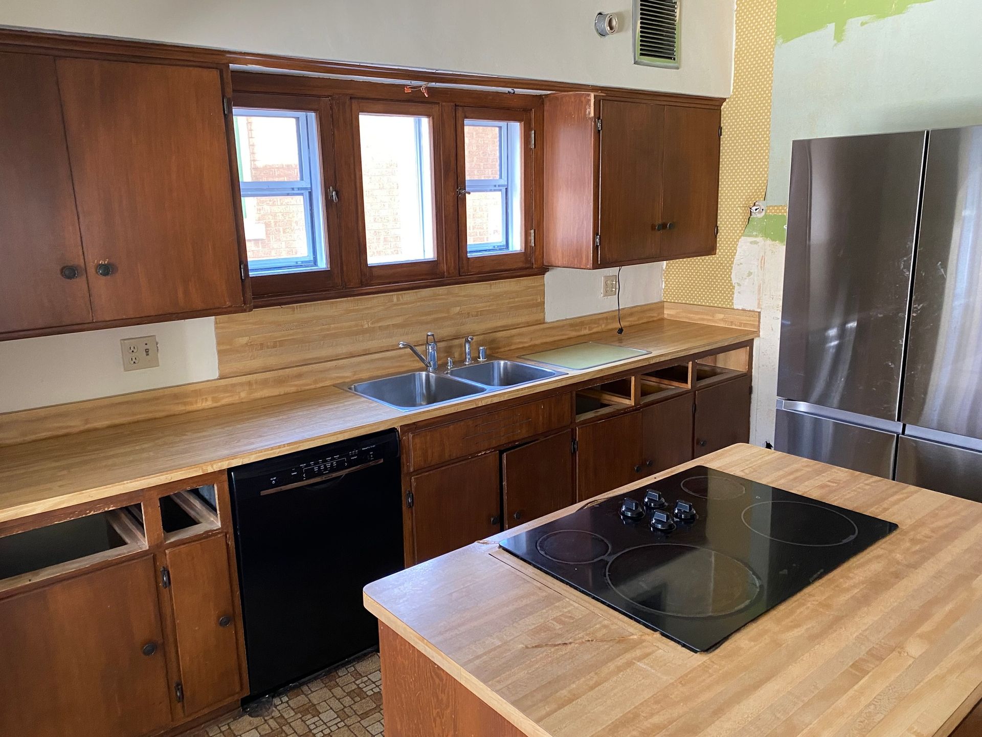 Kitchen with brown cabinets, light countertops, black appliances, and island with cooktop.