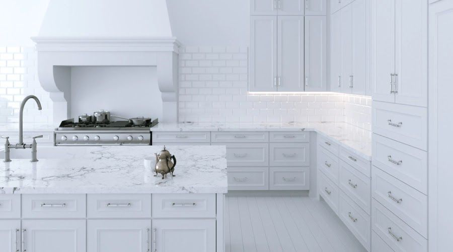White kitchen with island, stove, and cabinets; marble countertop; teapot.