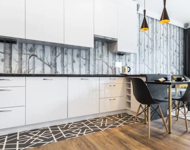 Modern white kitchen with black countertops, birch tree wallpaper, and patterned floor.