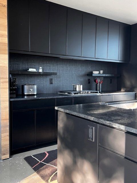 Black modern kitchen with black cabinets, countertop, and backsplash, with floating shelves.
