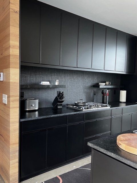 Modern kitchen with black cabinets, black backsplash, and wood paneling.