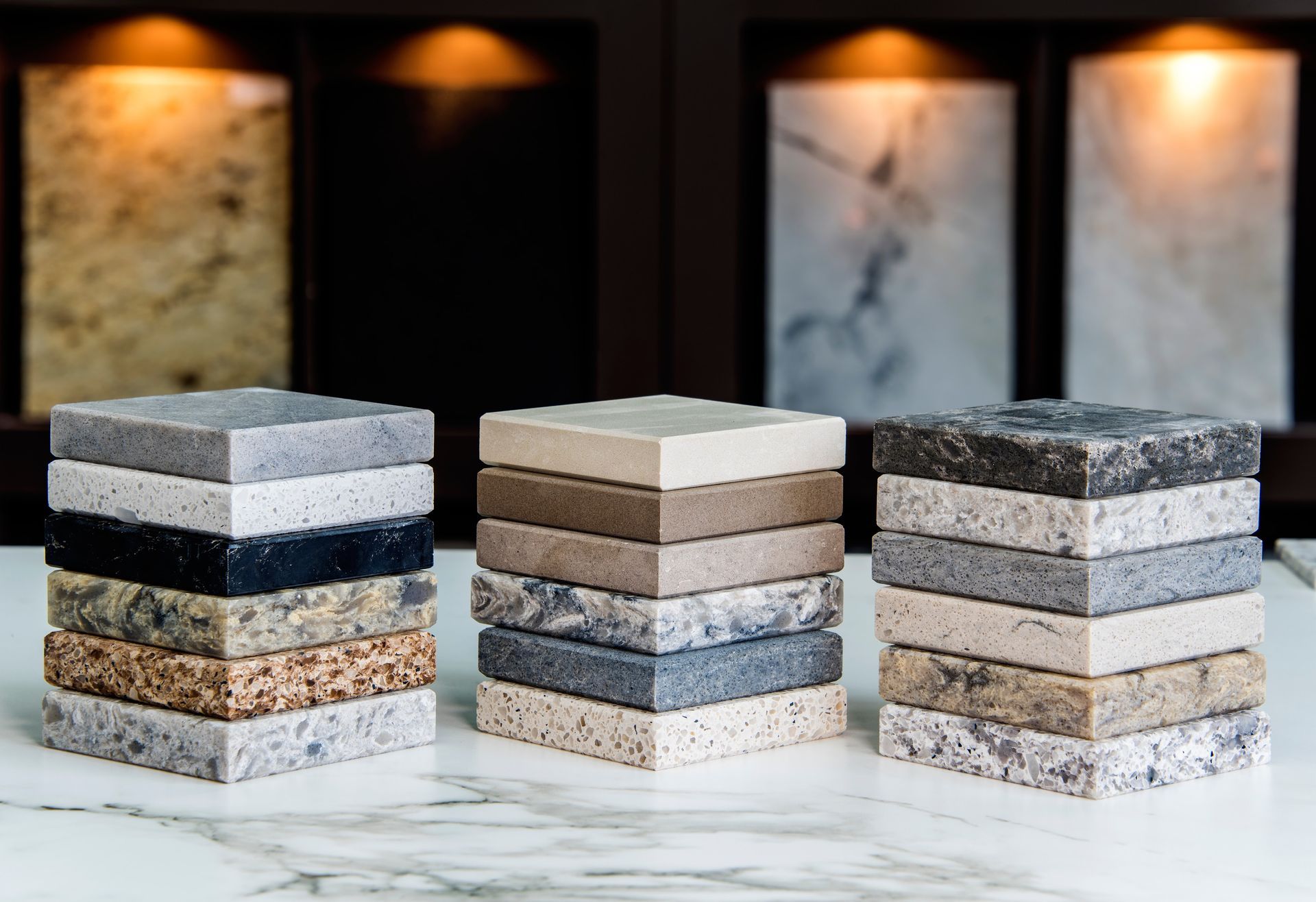 Three stacks of stone samples in front of background cabinet with samples lit up.