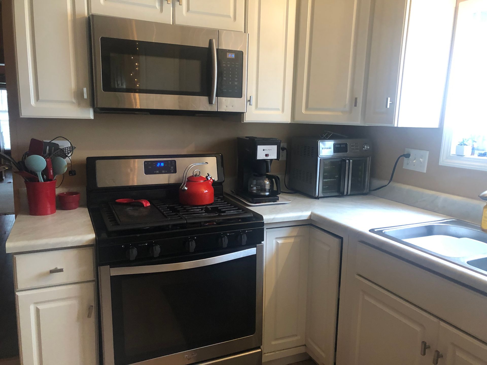Kitchen with stainless steel appliances: microwave, stove, coffee maker, and air fryer. White cabinets and countertops.