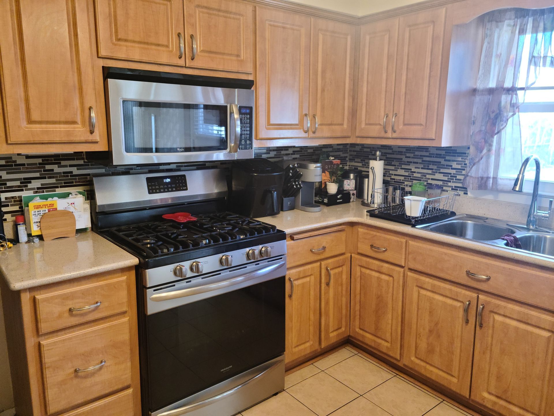 Kitchen with stainless steel appliances, light wood cabinets, and patterned backsplash.