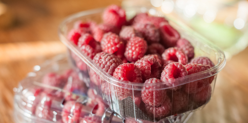 A plastic container filled with raspberries on a wooden table.