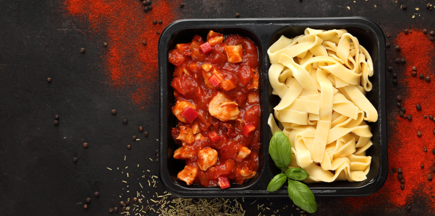 A plastic container filled with pasta and sauce on a table.