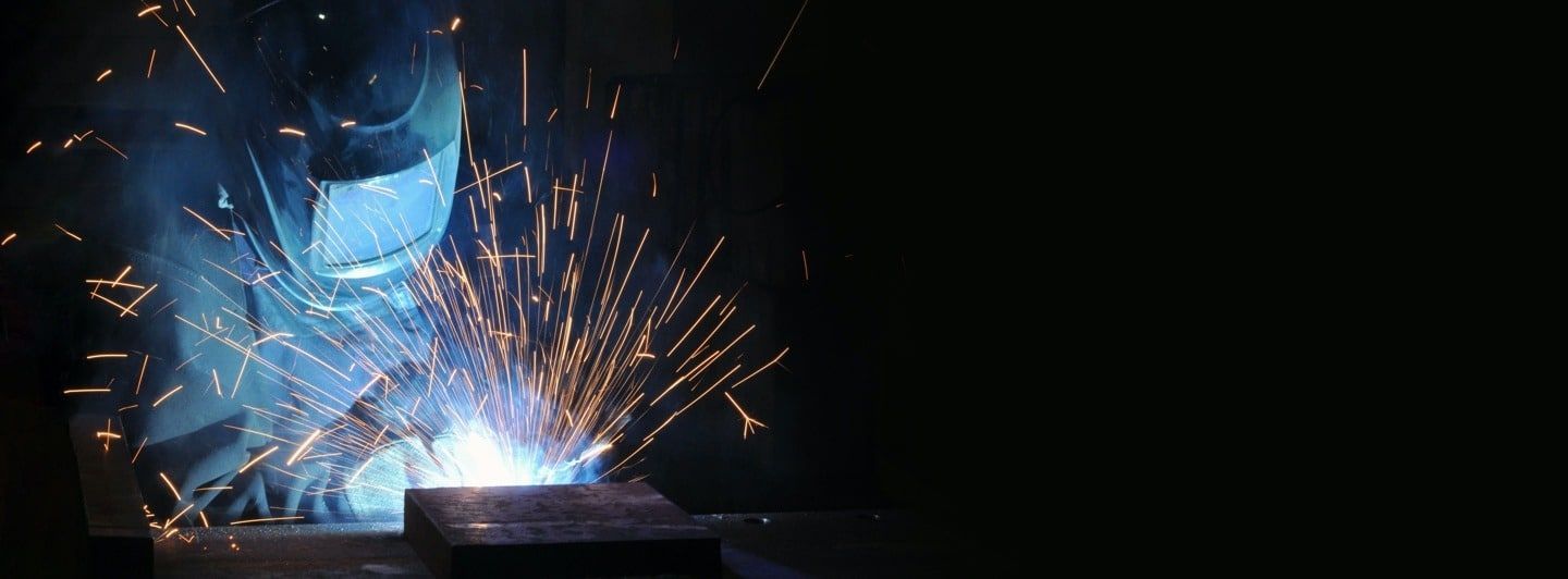 A man is welding a piece of metal in a dark room.