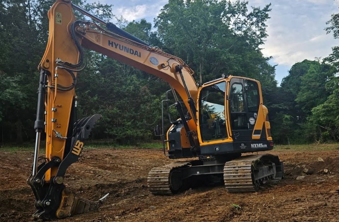 A yellow excavator is sitting in the middle of a dirt field.