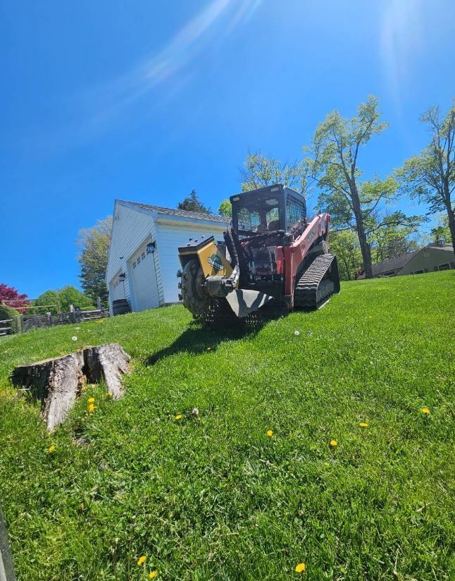 A tractor is cutting a tree stump in a lush green field.