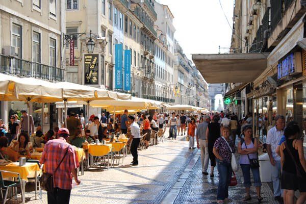 Rua da Baixa de Lisboa com muitas pessoas, lojas, farmácias e esplanadas