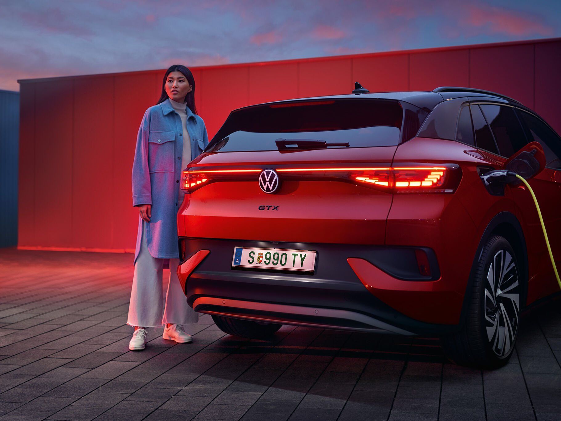 Mulher jovem em pé ao lado de um Volkswagen ID.4 GTX vermelho com carregamento elétrico
