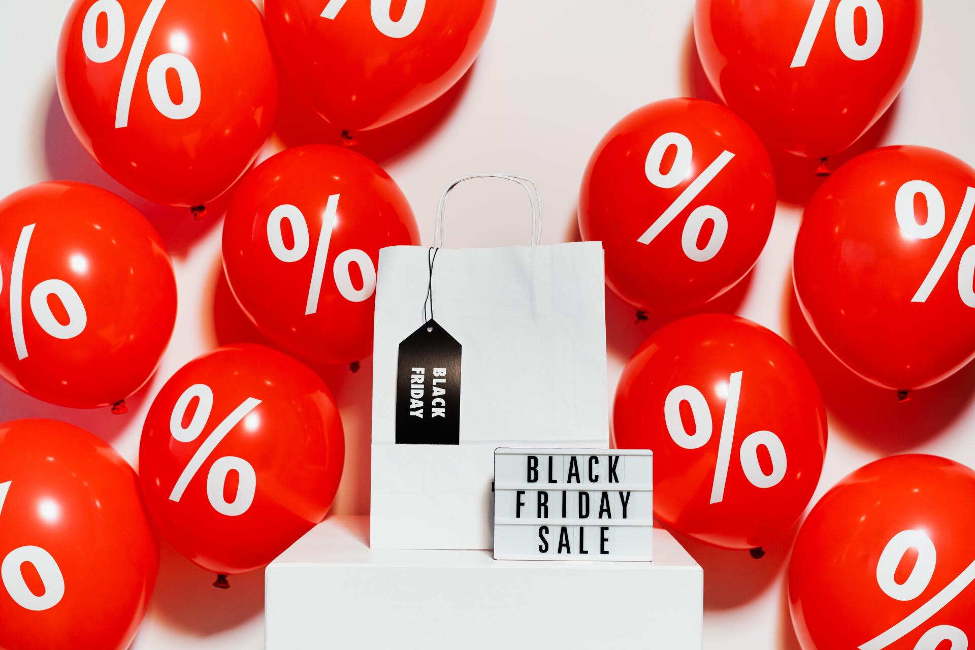 Balões vermelhos com símbolo de percentagem e saco de papel branco com cartaz Black Friday