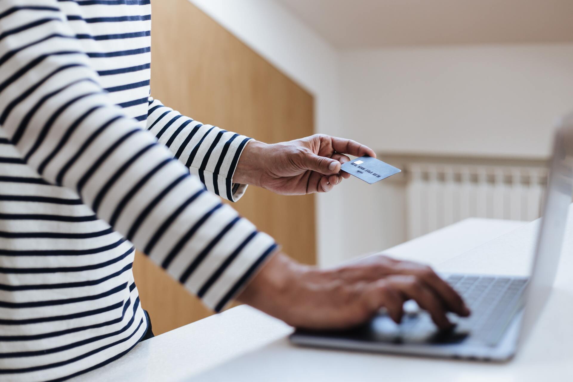 Pormenor de mulher a segurar cartão de crédito e a digitar no computador portátil