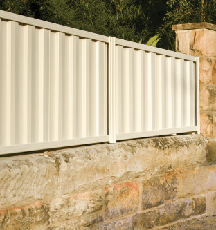 Cream-colored corrugated metal fence panels atop a weathered stone wall, in an outdoor setting.
