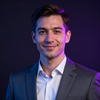 Studio portrait of a smiling man in a gray suit and white shirt, lit with blue and purple light