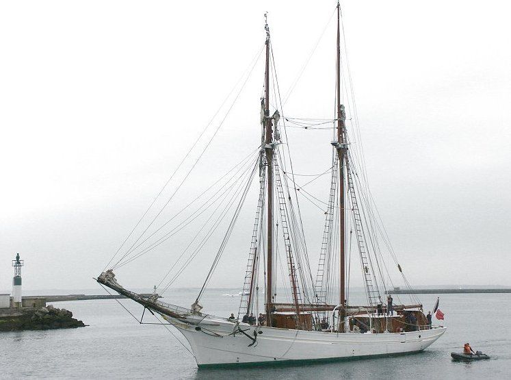 A large sailboat is docked in the water next to a small boat