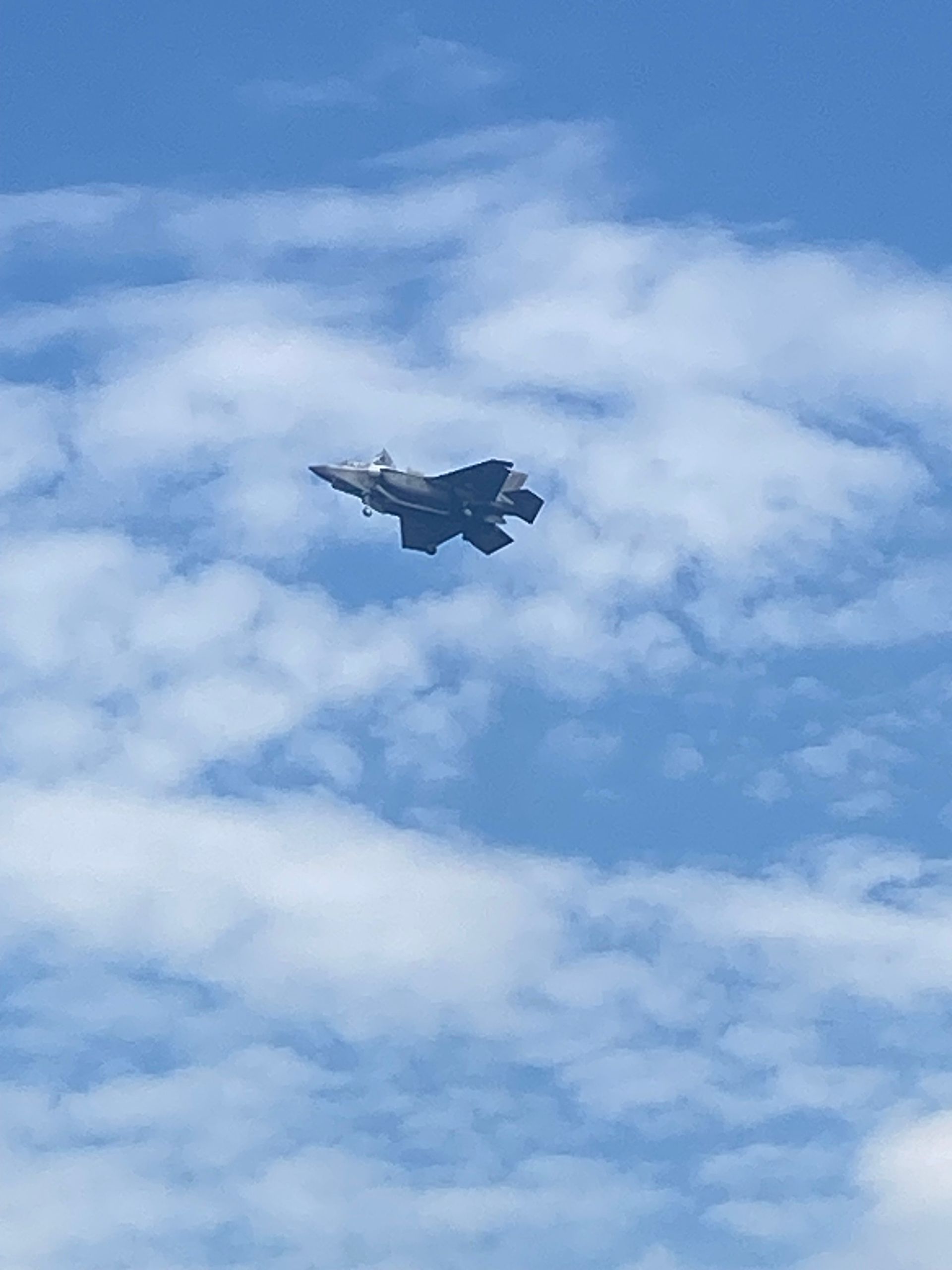 A fighter jet is flying through a cloudy blue sky