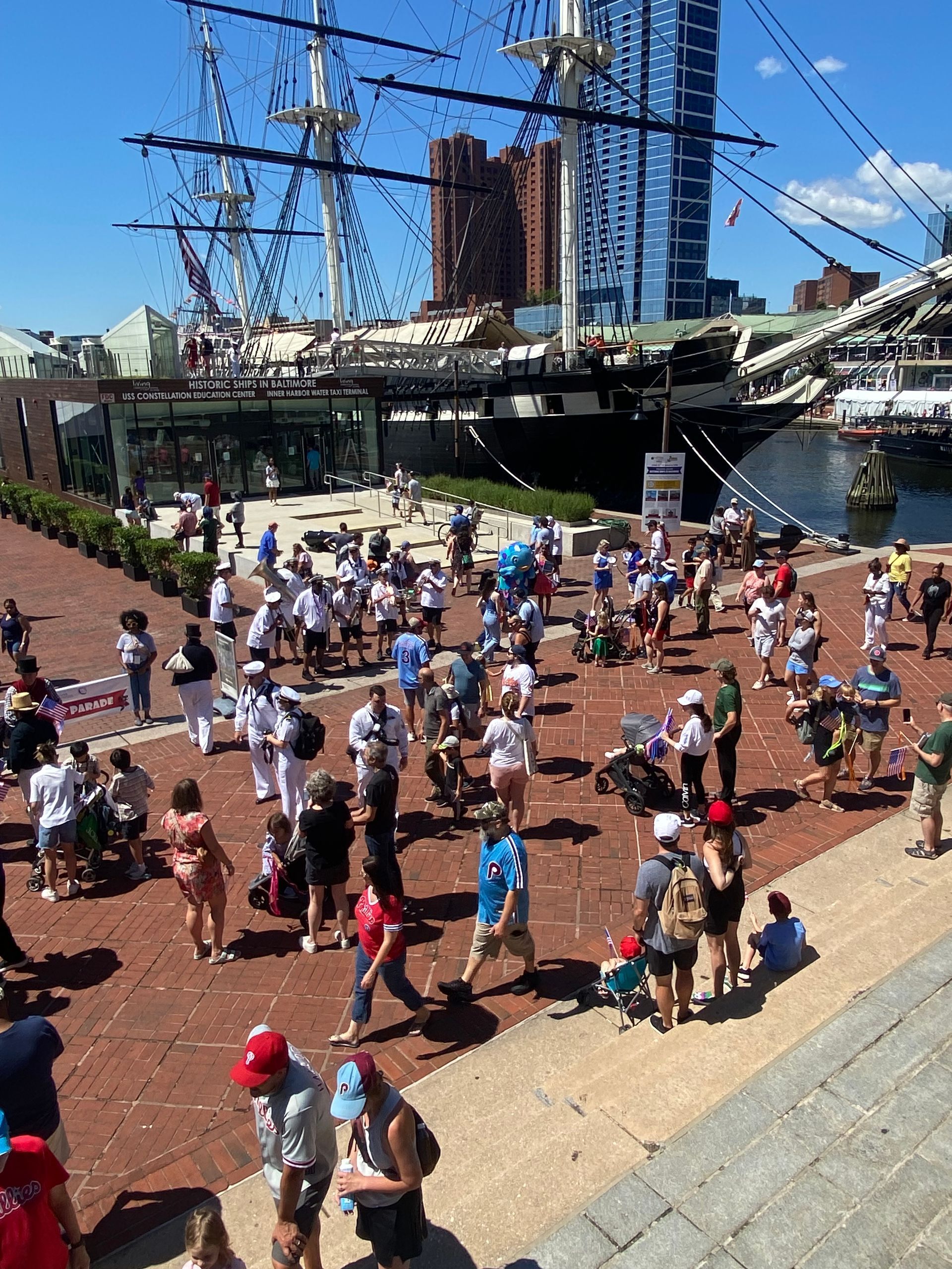 A large group of people are standing on a brick sidewalk in front of a large ship.