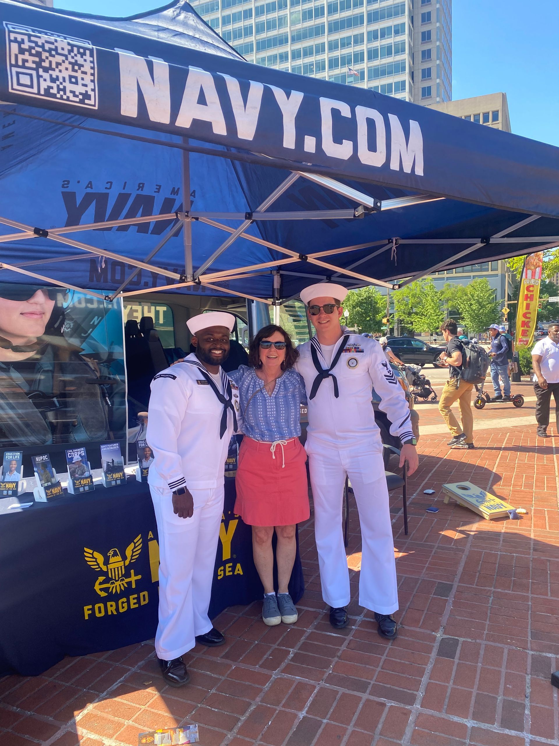 Three people are posing for a picture in front of a navy.com tent.