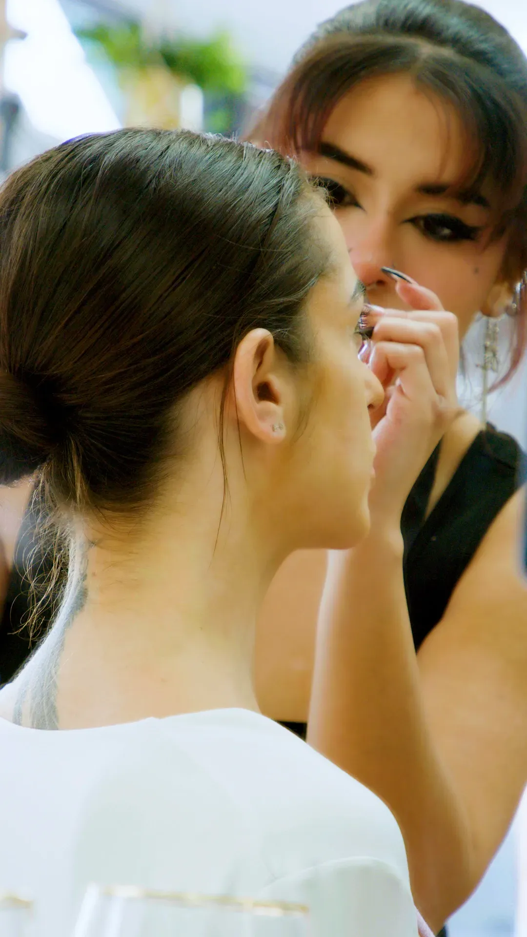 Woman having makeup applied; a person applies shadow to the client's eye in a bright setting.