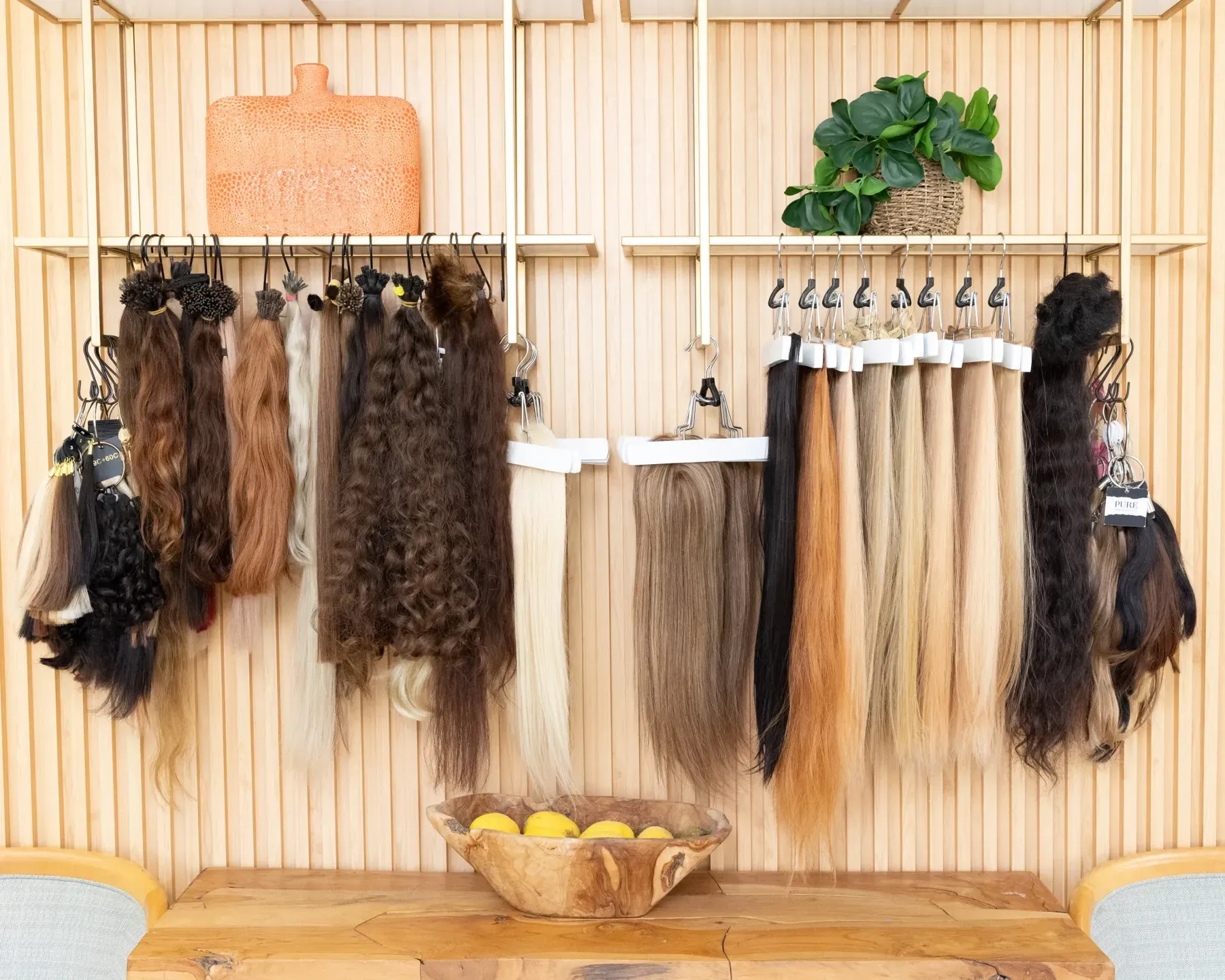 Hair extensions in various colors hanging on display against a light wood backdrop.