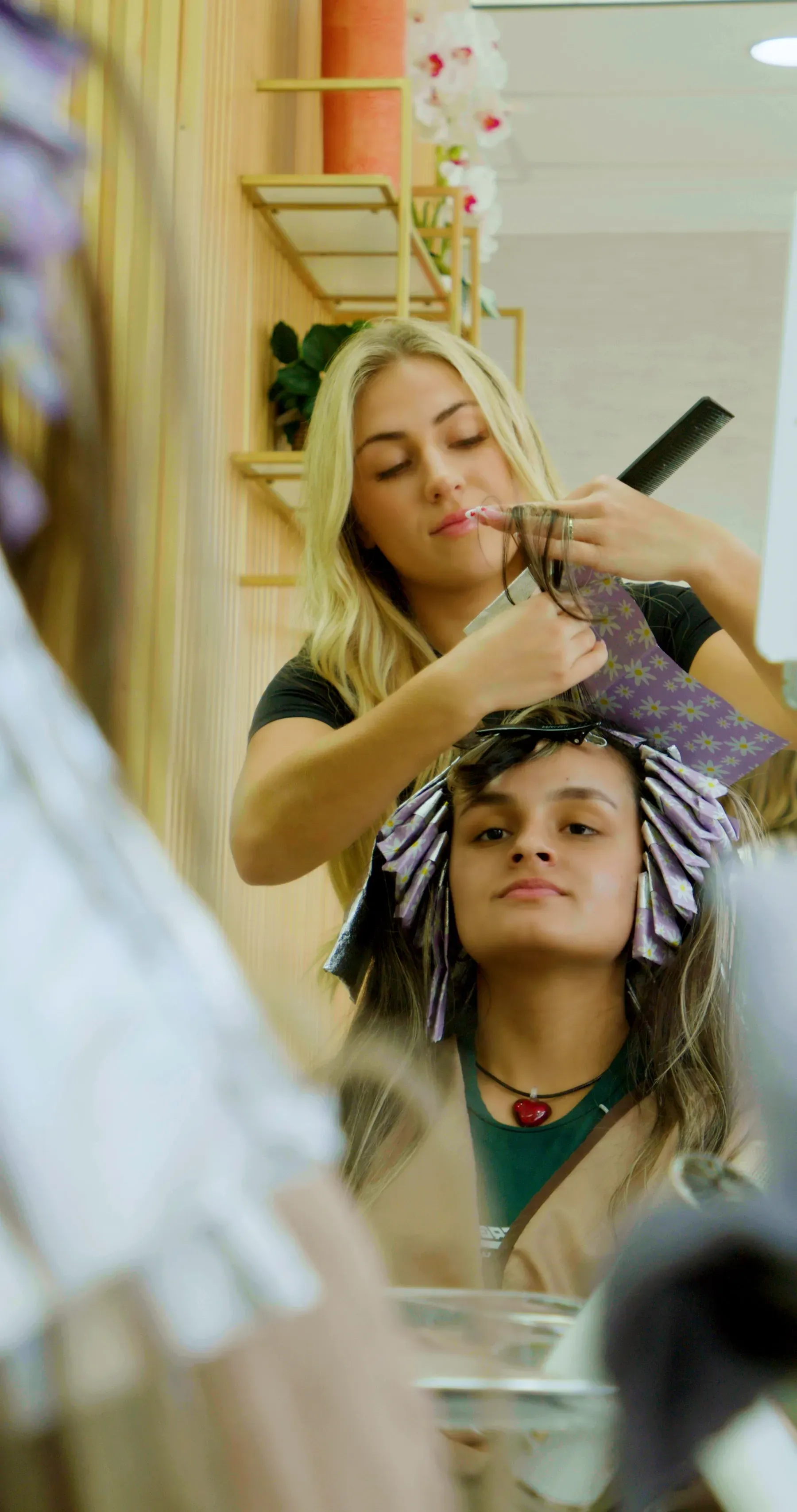 A hairstylist applying color to a client's hair in a salon. The client is looking at the mirror.