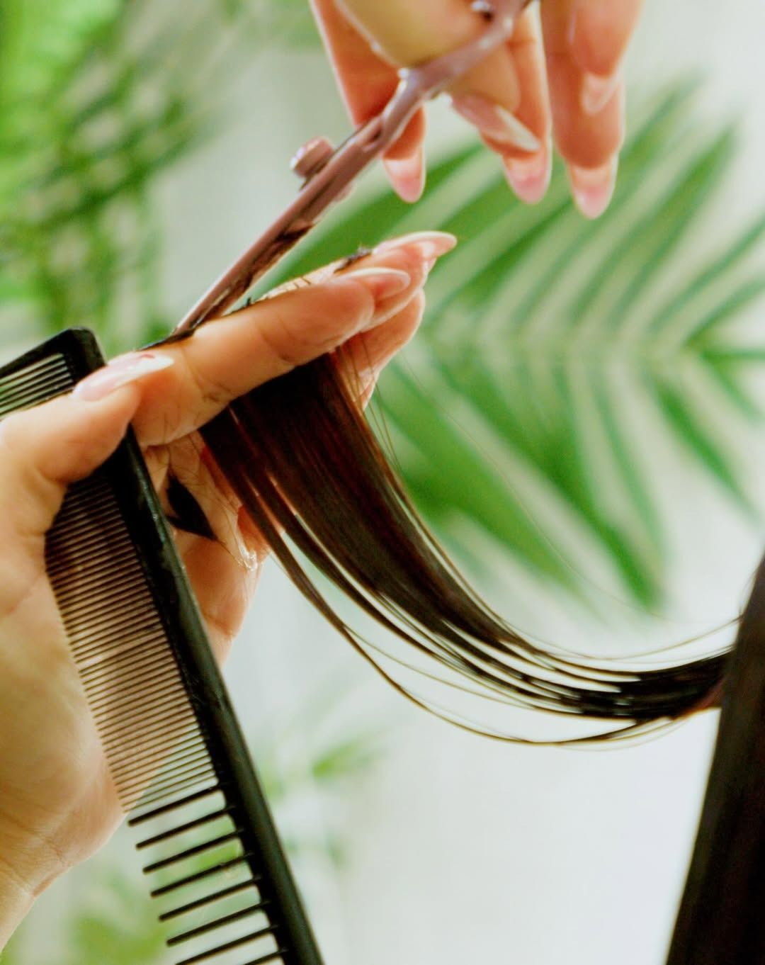 Hairdresser cutting long, dark hair with scissors and comb.