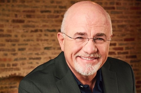 A bald man with glasses and a beard is smiling in front of a brick wall.