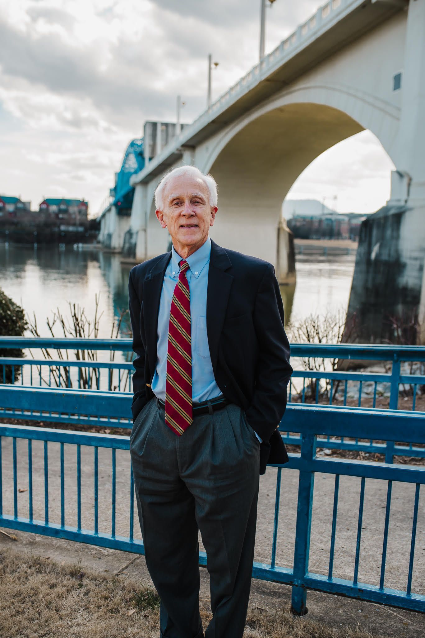 A man in a suit and tie is standing in front of a bridge.