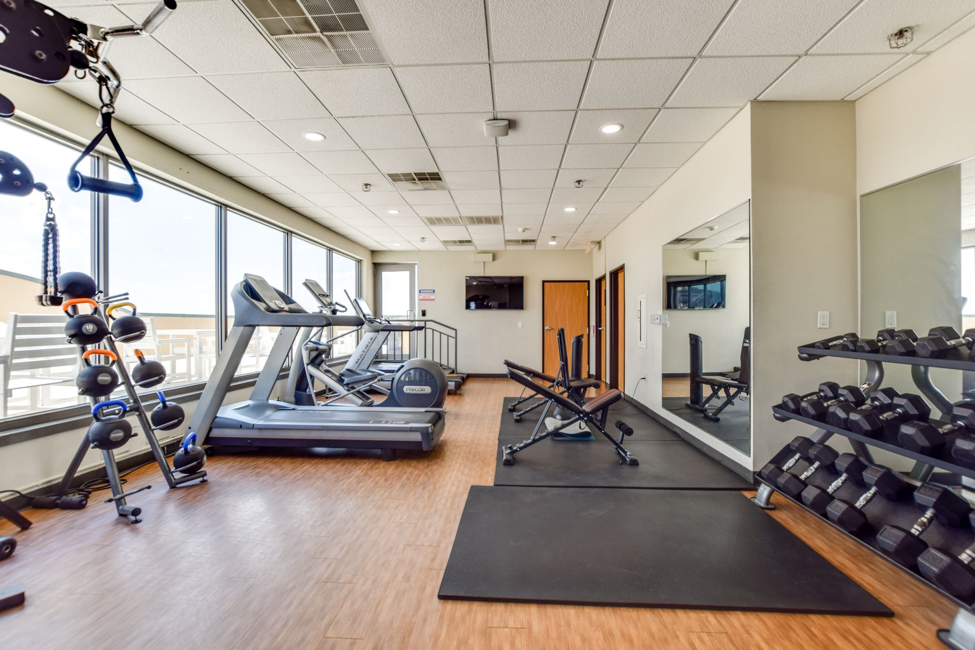A gym with treadmills , dumbbells , and a large mirror.