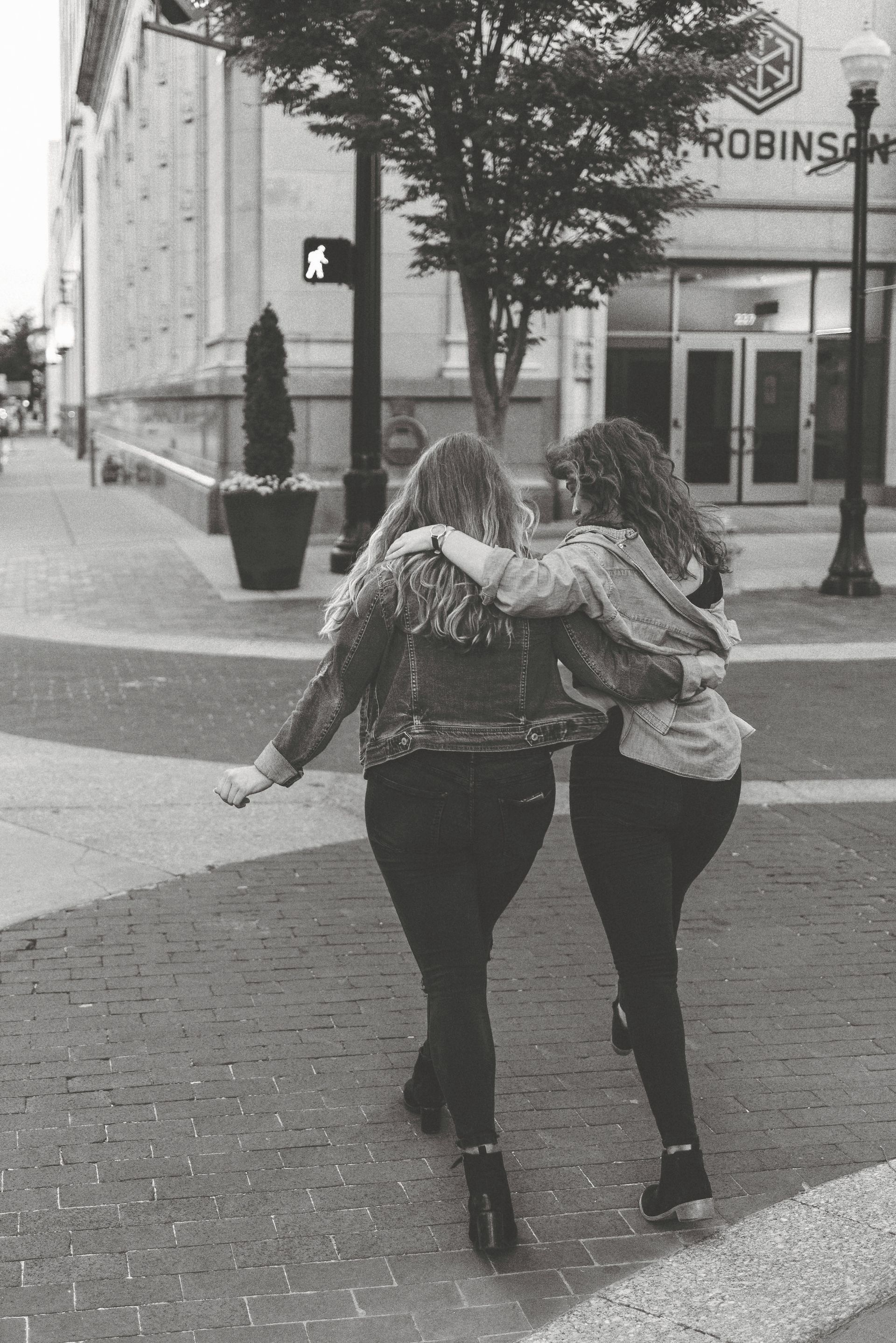 A black and white photo of two women hugging in front of a building that says robinsons