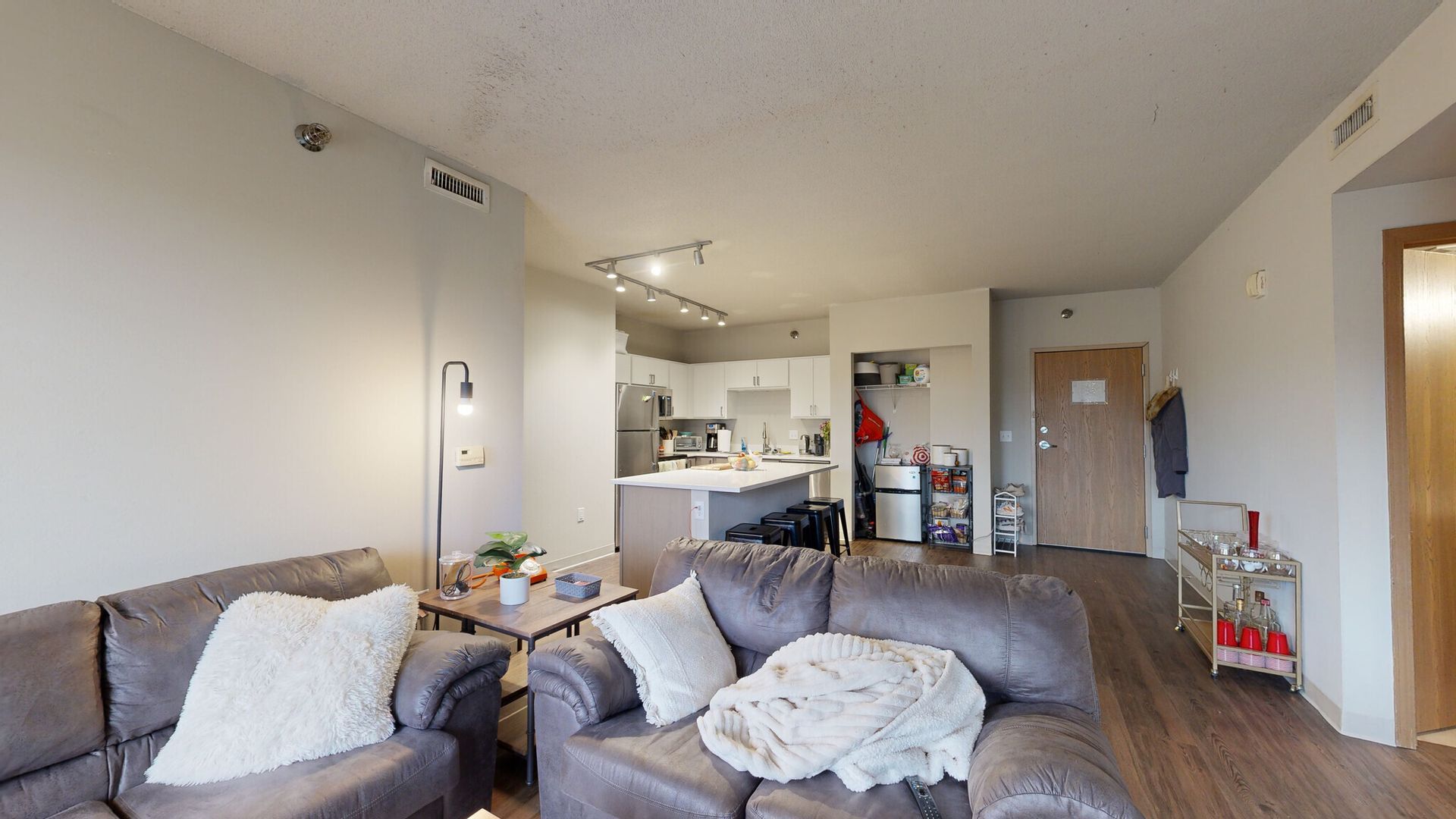 A living room with a couch and two chairs and a kitchen in the background.