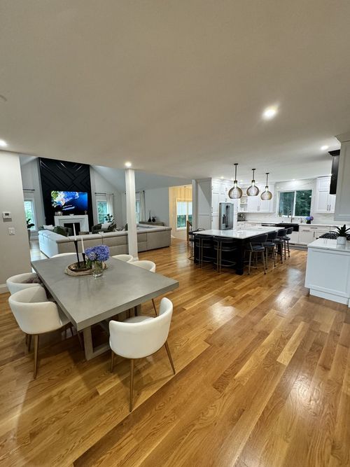 Open-concept kitchen and dining area with hardwood floors, a large island, and a dining table with white chairs.